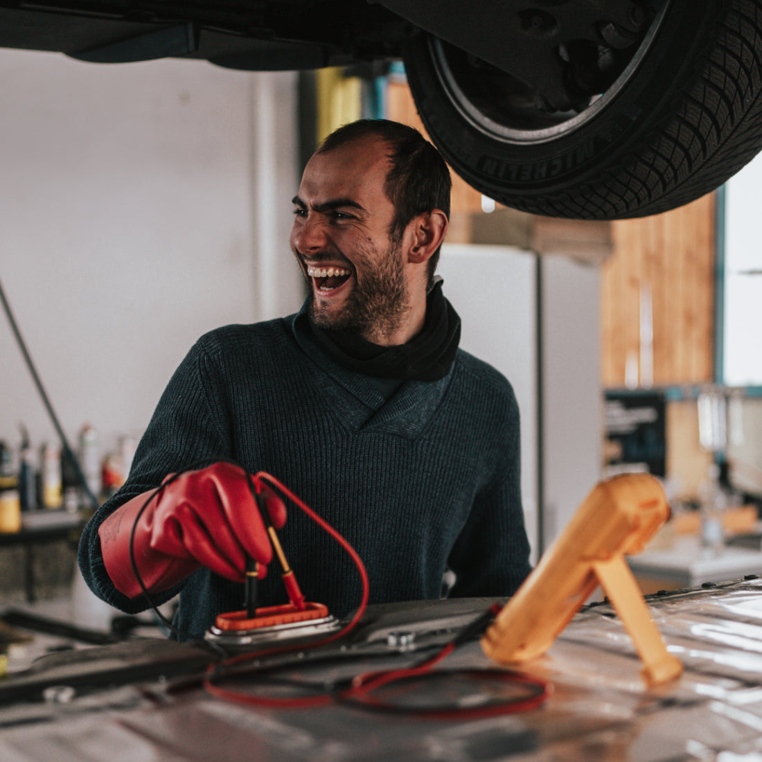 Lysander Parodi, Mitgründer von upVolt, prüft mit Messgerät und Schutzhandschuhen eine E-Auto-Batterie unter einem angehobenen Fahrzeug.