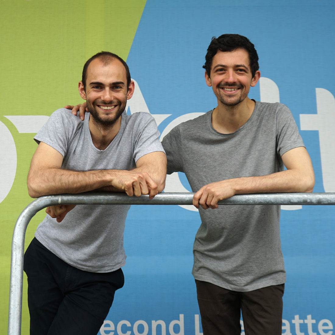 Die upVolt-Gründer Lukas Oppler und Lysander Parodi, lächelnd an ein Geländer gelehnt, vor dem grün-blauen upVolt-Banner.