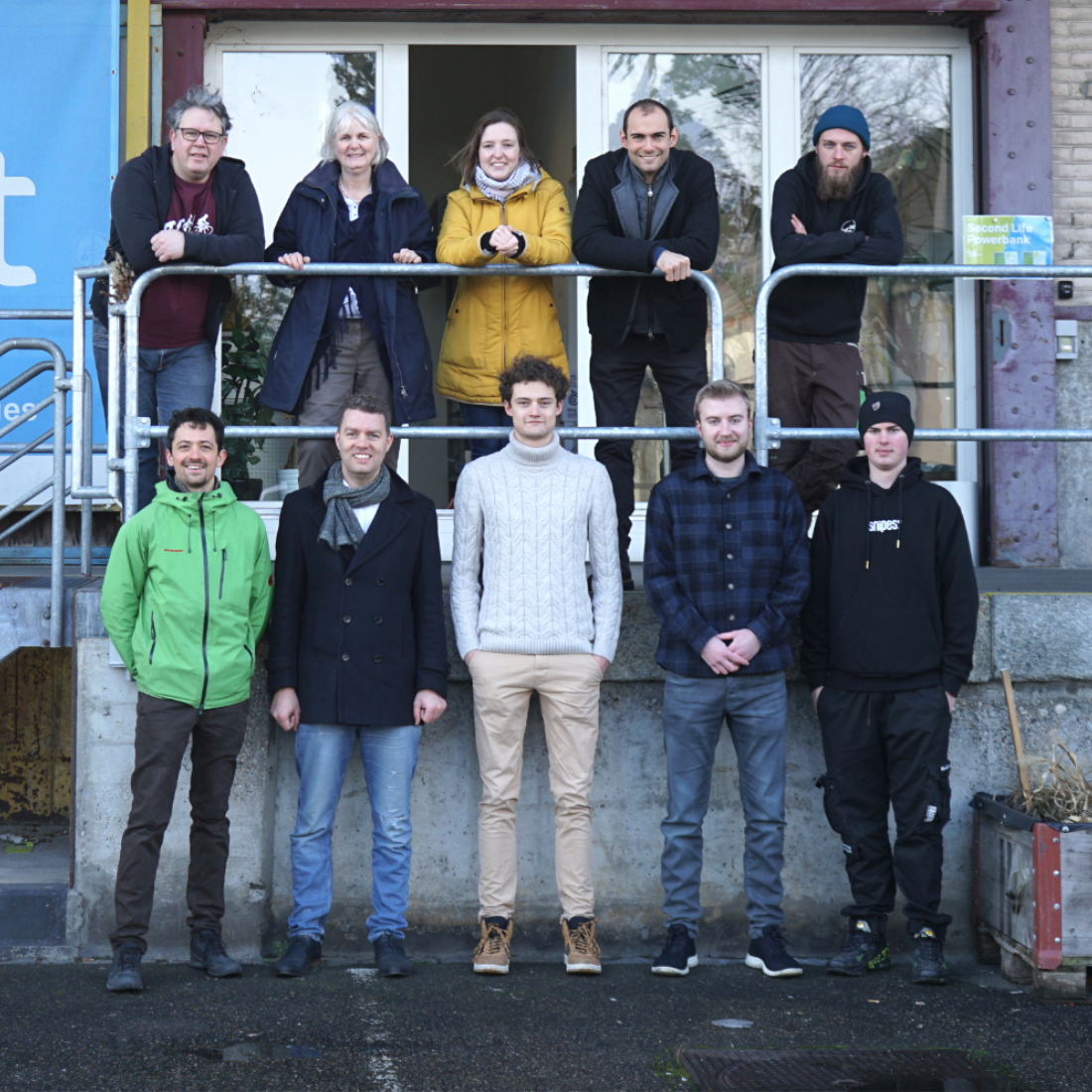 Das rund zehnköpfige upVolt-Team steht lächelnd auf der Treppe vor dem Werkstatt-Eingang in Basel.